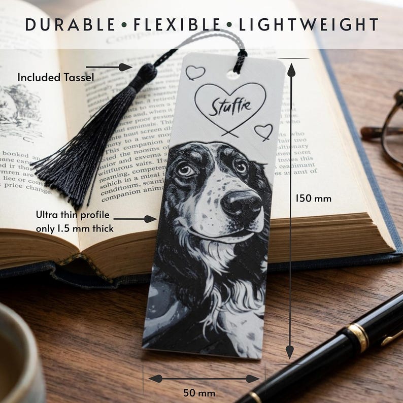 May include: A white rectangular bookmark featuring a black and white illustration of a dog, the word Stuffie inside a heart, and two smaller hearts. It includes a black tassel, measures 150 mm by 50 mm, and has an ultra thin 1.5 mm profile.