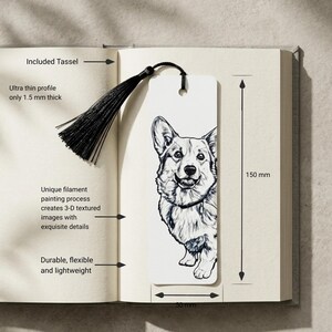 May include: A white rectangular bookmark featuring a black and white line drawing of a Corgi dog. The bookmark includes a black tassel attached through a hole at the top. It measures 150 mm in height and 50 mm in width, with a 1.5 mm thickness.
