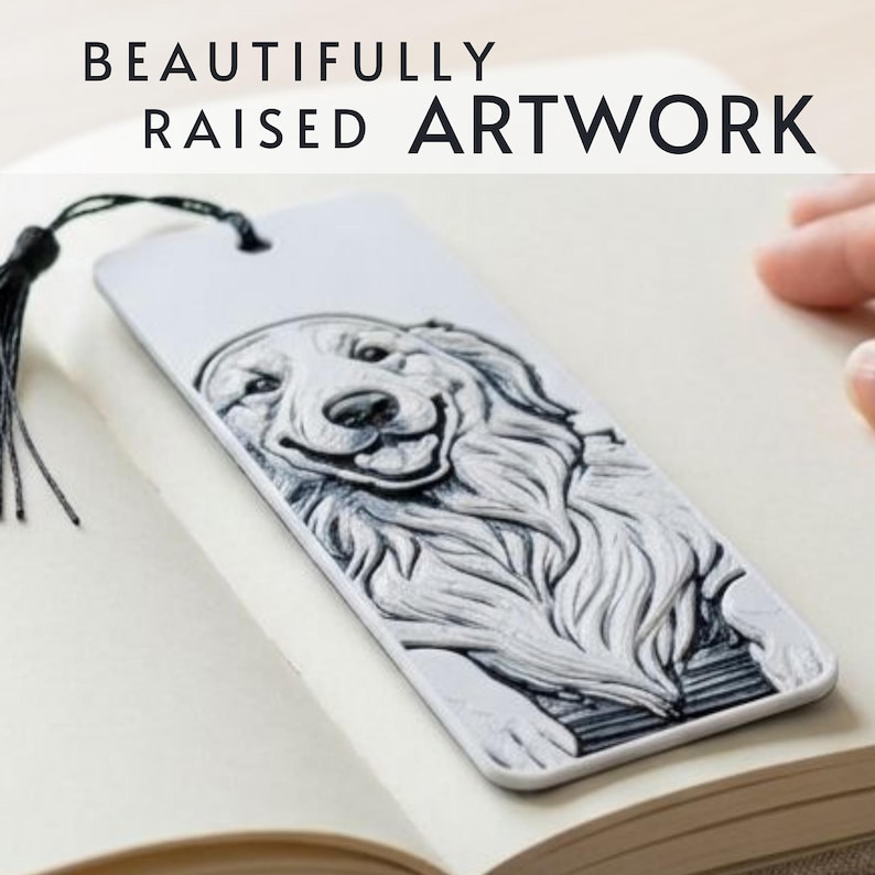 May include: A white rectangular bookmark featuring a raised black and white illustration of a golden retriever dog. The bookmark includes a black tassel and the text BEAUTIFULLY RAISED ARTWORK printed in black at the top of the image.