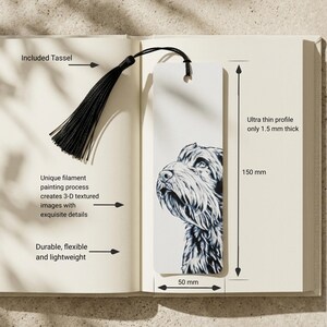 May include: A rectangular white bookmark featuring a detailed black and white illustration of a dog's head. The bookmark includes a black tassel attached to the top hole. It measures 150 mm in height, 50 mm in width, and 1.5 mm in thickness.