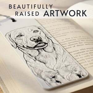 May include: A white rectangular bookmark featuring a raised, black-ink line drawing of a Labrador retriever dog. The bookmark has a black string at the top and displays the text BEAUTIFULLY RAISED ARTWORK at the top of the image.