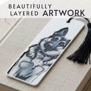 May include: A white rectangular bookmark featuring a layered, three-dimensional relief illustration of a German Shepherd dog in shades of gray and white. The bookmark includes a black tassel attached to the top and the text BEAUTIFULLY LAYERED ARTWORK.