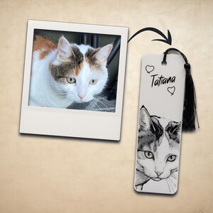 May include: A rectangular bookmark featuring a black and white illustration of a calico cat, the name Tatiana, two small heart outlines, and a black tassel attached to the top. Next to it is a square photograph of the same calico cat.