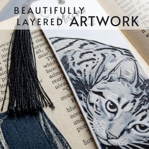 May include: A white bookmark featuring a detailed black and white engraved illustration of a cat's face. The bookmark includes a black tassel attached to the top and displays the text BEAUTIFULLY LAYERED ARTWORK across the upper portion.