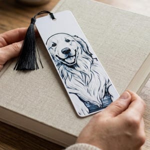 May include: A rectangular white bookmark featuring a detailed black and white ink illustration of a smiling golden retriever dog. The bookmark has a hole at the top with a black thread tassel attached, and the dog is depicted from the chest up.