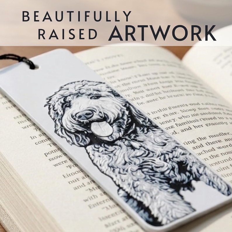 May include: A white rectangular bookmark featuring a black and white illustration of a curly-haired dog with its tongue out. The bookmark has a black string at the top and the text BEAUTIFULLY RAISED ARTWORK is printed above the bookmark.