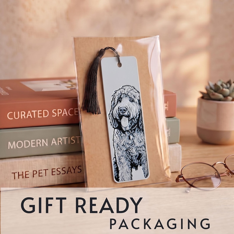 May include: A rectangular bookmark featuring a black and white illustration of a curly-haired dog with its tongue out. The bookmark is made of a light-colored material, includes a dark brown tassel at the top, and is enclosed in clear packaging.