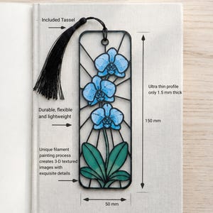 May include: A rectangular black bookmark featuring a blue orchid design with green leaves. It includes a black tassel, measures 150 mm by 50 mm, and has an ultra thin profile of 1.5 mm. The text reads: Included Tassel, Durable, flexible and lightweight, Unique filament painting process creates 3-D textured images with exquisite details, Ultra thin profile only 1.5 mm thick, 150 mm, 50 mm.