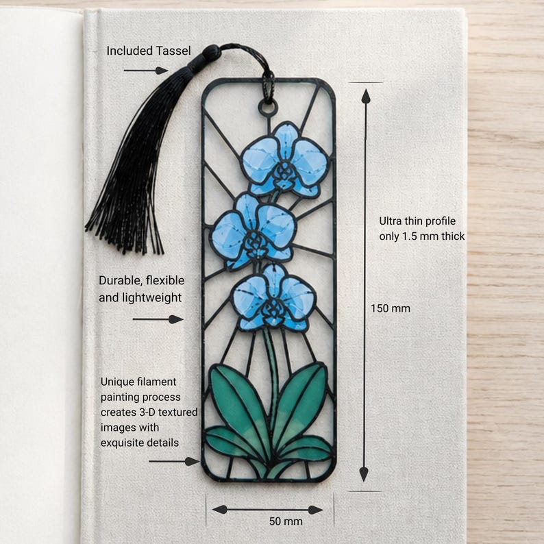 May include: A rectangular black bookmark featuring a blue orchid design with green leaves. It includes a black tassel, measures 150 mm by 50 mm, and has an ultra thin profile of 1.5 mm. The text reads: Included Tassel, Durable, flexible and lightweight, Unique filament painting process creates 3-D textured images with exquisite details, Ultra thin profile only 1.5 mm thick, 150 mm, 50 mm.