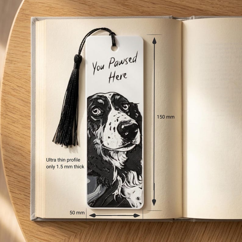 May include: A white rectangular bookmark featuring a black and white illustration of a dog and the text "You Pawsed Here". It includes a black tassel, measures 150 mm by 50 mm, and has an ultra thin profile of 1.5 mm thick.