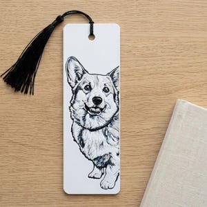 May include: A white rectangular bookmark featuring a detailed black and white ink illustration of a Corgi dog. The bookmark has a hole at the top with a black thread tassel attached, hanging from a thin black cord loop.