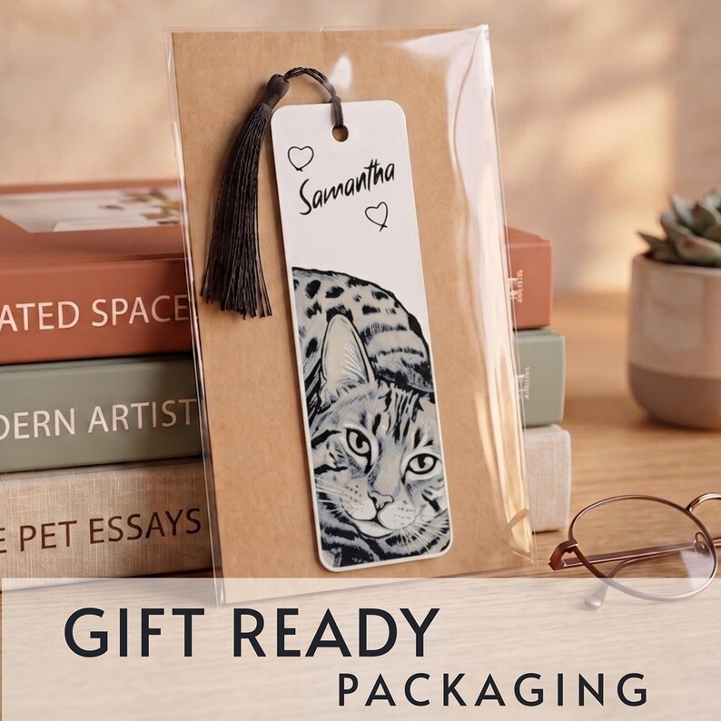 May include: A white rectangular bookmark featuring a black and white illustration of a cat's face, the name Samantha, and two small heart outlines. A dark gray tassel is attached to the top, and the bookmark is enclosed in clear plastic packaging.