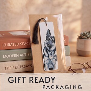 May include: A rectangular white bookmark featuring a detailed illustration of a German Shepherd dog. The bookmark has a hole at the top with a dark brown tassel attached and is enclosed in a clear plastic sleeve for protection and presentation.