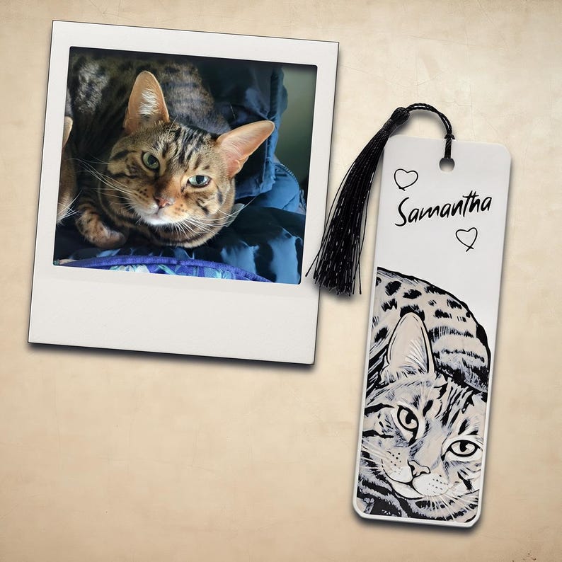 May include: A rectangular bookmark featuring a black and white illustration of a tabby cat, the name "Samantha" in black script, two small heart outlines, and a black tassel attached to the top through a circular hole, next to a square photo.