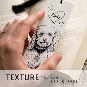 May include: A white rectangular bookmark featuring a detailed black and white illustration of a curly-haired dog wearing a collar with a tag. The top of the bookmark displays the name Daisy written inside a heart outline with two smaller hearts.