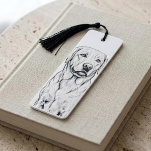 May include: A rectangular white bookmark featuring a detailed black and white line drawing of a Labrador Retriever dog. The bookmark has a hole at the top with a black silk tassel attached, providing a decorative accent to the illustrated canine.