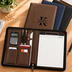 May include: A brown leather portfolio with a zip closure, featuring a calculator, two pens, card slots, and a notepad labelled MEMO. The front cover is personalised with a large letter K and the name KAAMIL in black ink.