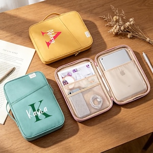 May include: Three personalised zippered cases in yellow, teal, and pink, with handles. The yellow case has "Abbey" and a large red "A". The teal case has "Kayla" and a green "K". The pink case is open, revealing a tablet and accessories.