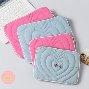 May include: Three quilted laptop sleeves in pink and blue with a heart design. The smallest sleeve has the name "AMY" embroidered on the front.