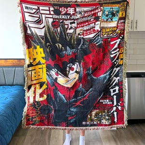 Könnte beinhalten: Eine rot-schwarze Decke mit einer Manga-Illustration eines Charakters mit stacheligen Haaren und einem entschlossenen Gesichtsausdruck. Die Decke hat japanischen Text und einen Fransenbesatz.