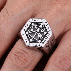 May include: A silver hexagonal ring with a geometric design at its centre. The ring has runes around the edges and is worn on a finger. This is a piece of jewellery.