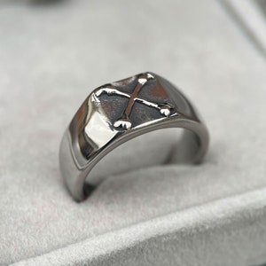 May include: A silver ring with a cross design. The ring is made of metal and has a polished finish.