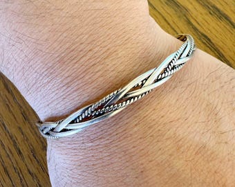 May include: A silver braided bangle bracelet with a woven design.