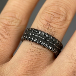 Puede incluir: Un anillo de plata con un diseño texturizado y en capas. El anillo se lleva en un dedo.