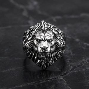 May include: A silver-colored ring featuring a detailed lion's head design. The ring showcases the lion's mane, facial features, and overall form. The ring is a bold statement piece.
