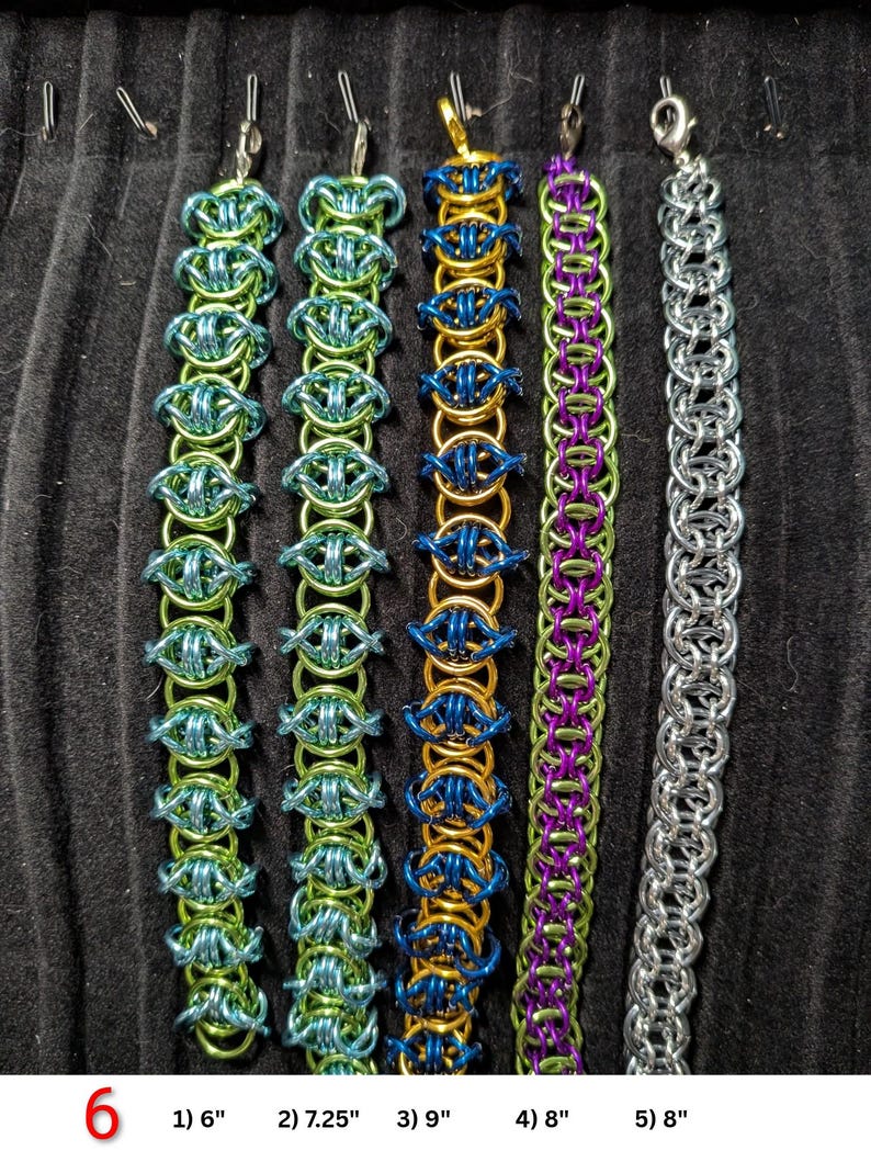 May include: Five chainmaille bracelets with lobster claw clasps. From left to right: a 6-inch teal and light green bracelet, a 7.25-inch light green and teal bracelet, a 9-inch gold and blue bracelet, an 8-inch purple and green bracelet, and an 8-inch silver bracelet.