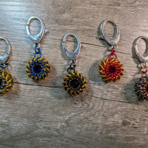 May include: Five handmade keychains with silver-colored clasps and spiral-shaped pendants. The pendants are in various colors, including gold, blue, black, red, and bronze. The keychains are displayed on a wooden surface.