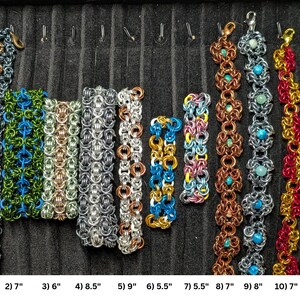 May include: Eleven chainmaille bracelets in various colors and patterns, including metallic, blue, green, red, and gold tones. Each bracelet features a lobster clasp and is labeled with a number and length in inches, ranging from 5.5 to 9 inches.