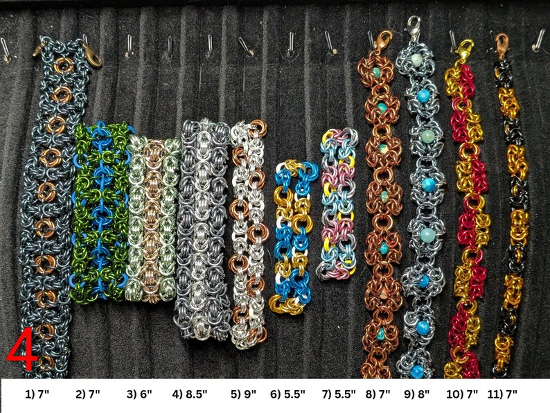 May include: Eleven chainmaille bracelets in various colors and patterns, including metallic, blue, green, red, and gold tones. Each bracelet features a lobster clasp and is labeled with a number and length in inches, ranging from 5.5 to 9 inches.