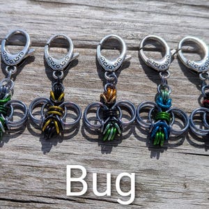 May include: Five handmade bug-shaped keychains with silver-tone clasps. Each bug is crafted from interwoven metal rings and colorful wire in green, yellow, orange, blue, and red. The word "Bug" is displayed below.