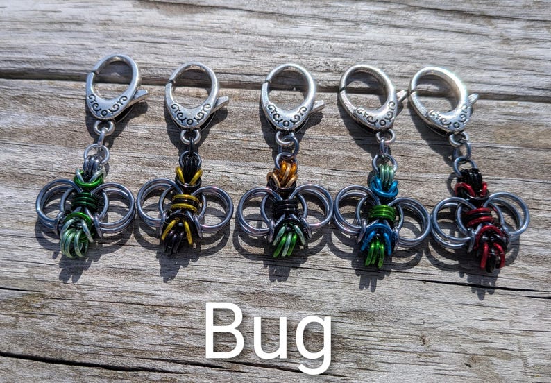 May include: Five handmade bug-shaped keychains with silver-tone clasps. Each bug is crafted from interwoven metal rings and colorful wire in green, yellow, orange, blue, and red. The word "Bug" is displayed below.