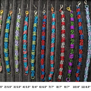 May include: Eleven chainmaille bracelets in various color combinations including pink, green, blue, red, silver, and purple. Each bracelet features a lobster claw clasp and is numbered 1 through 11 with lengths ranging from 5.5 inches to 8.5 inches.
