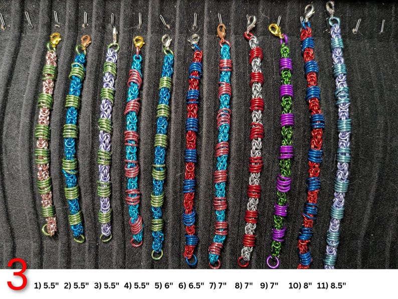 May include: Eleven chainmaille bracelets in various color combinations including pink, green, blue, red, silver, and purple. Each bracelet features a lobster claw clasp and is numbered 1 through 11 with lengths ranging from 5.5 inches to 8.5 inches.