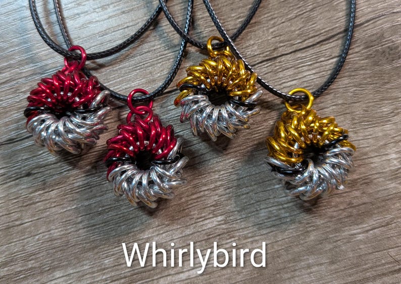 May include: Four handmade pendant necklaces with circular, woven designs. Two are red and silver, and two are gold and silver. The pendants are suspended from black cords. The word "Whirlybird" is displayed in white text at the bottom.