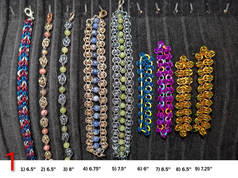 May include: Nine chainmaille bracelets arranged vertically. 1) Red, blue, silver 6.5 inches. 2) Pink, silver 6.5 inches. 3) Green, silver 8 inches. 4) Blue, gold 6.75 inches. 5) Green, silver 7.5 inches. 6) Blue, yellow 6 inches. 7) Purple, orange 8.5 inches. 8) Gold, green 6.5 inches. 9) Gold, green 7.25 inches.
