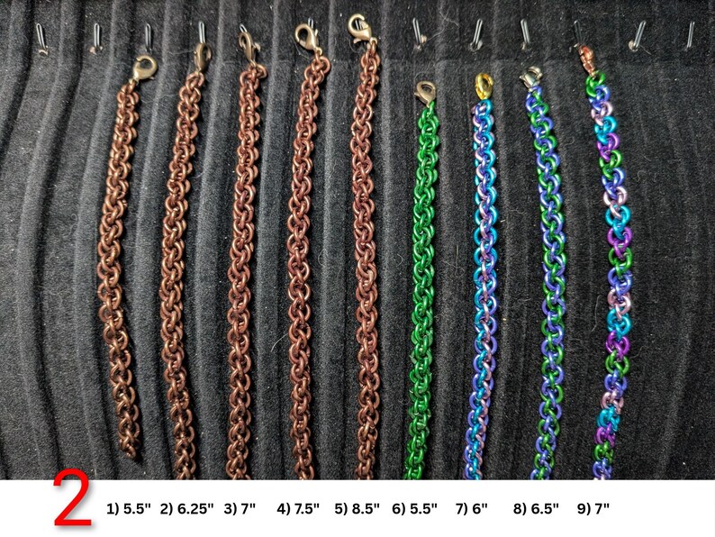 May include: Nine chainmaille bracelets with lobster claw clasps, arranged vertically. Five are copper-colored, one is green, one is blue and green, one is blue and purple, and one is a multi-colored gradient. Lengths range from 5.5 to 8.5 inches.