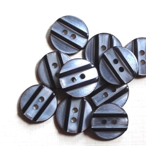 May include: A group of ten round, two-hole buttons with a black and white striped design. The buttons are made of a shiny, pearlescent material.