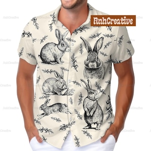 Puede incluir: Una camisa beige de botones con manga corta que presenta un patrón repetido de ilustraciones de conejos en blanco y negro. La camisa tiene cuello y cierre de botones.