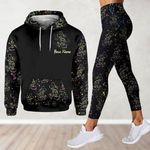 May include: Black hoodie and leggings set featuring a colourful Mickey Mouse print. The hoodie has a drawstring hood and a kangaroo pocket. The leggings are full-length and have a comfortable fit. The set features the text "Your Name" on the hoodie.
