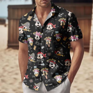 Może przedstawiać: Czarna koszula z krótkim rękawem z powtarzającym się wzorem postaci piratów z kreskówek, w tym Myszki Miki, Myszki Minnie, Kaczora Donalda i Plutona. Koszula ma klasyczny kołnierz i jest noszona przez osobę.