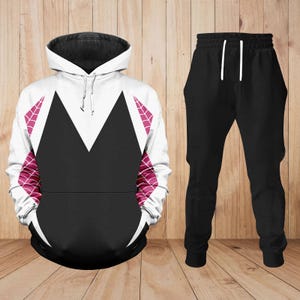 May include: A black and white hooded sweatshirt and black tracksuit bottoms set. The sweatshirt has a white upper section with a black chevron design and pink web-like accents. The black tracksuit bottoms have a white drawstring.
