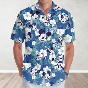 Może przedstawiać: Niebieska koszula z krótkim rękawem zapinana na guziki z tropikalnym nadrukiem przedstawiającym Myszki Miki, Minnie i Donalda. Nadruk zawiera również białe kwiaty hibiskusa i zielone liście.