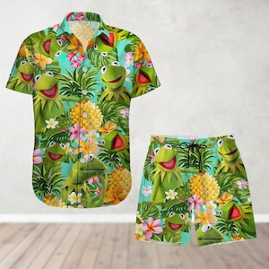 May include: A green and blue tropical print button-up shirt and matching swim trunks featuring a cartoon frog character. The shirt has a collar and short sleeves. The swim trunks have an elastic waistband and a drawstring.