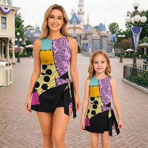 May include: Two sleeveless dresses featuring a patchwork design with light blue, yellow, and purple sections adorned with black circles, swirls, and triangles. The skirts have a black wrap-style overlay with a side tie and visible stitch details.