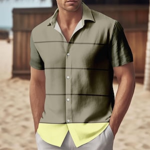 May include: A short-sleeved button-down shirt in olive green with horizontal black stripes. The bottom panel is light yellow. The shirt has a classic collar and is worn with light gray pants. The background shows a beach scene.
