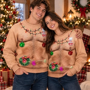 May include: Two beige crewneck sweatshirts featuring a realistic, high-definition print of a hairy chest. The design includes a string of colourful Christmas lights draped across the chest, hanging ornaments on the nipples, and a wreath.